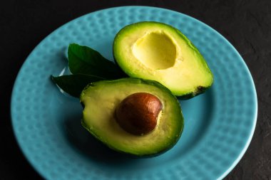Siyah tahtadaki mavi seramik tabakta taze avokado ikiye bölünmüş. Sağlıklı beslenme konsepti. Yemek fotoğrafçılığı