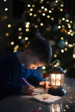 Küçük çocuk geceleri Noel ağacı için el yapımı süslemeler yapıyor. Arka planda ışıklar olan Noel ağacı. Kış tatili kavramı