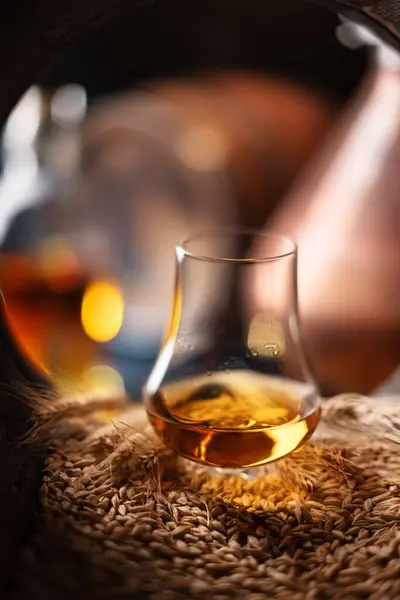 一杯威士忌在老橡木桶里 背景上的铜羊肉蒸馏器 传统的酒精酿酒厂概念 图库图片