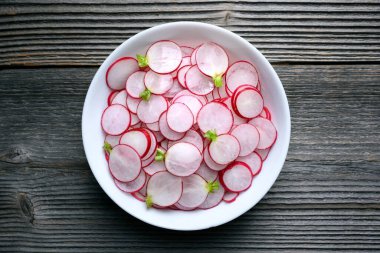 Thin radish slices in a white plate on rustic wooden table. Vegetable salad. Food photography