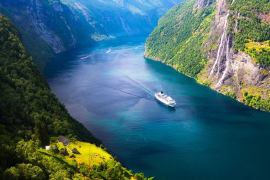 Norveç 'in batısındaki Geiranger köyü yakınlarındaki Sunnylvsfjorden fiyordunun açık mavi sularında büyük bir yolcu gemisi. Arka planda Yedi Kız Kardeş Şelalesi