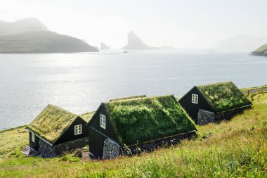 Köy otobüsündeki geleneksel çim kaplı kır evleri. Arka planda Drangarnir ve Tindholmur deniz yığınları var. Vagar Adası, Faroe Adaları, Danimarka. Peyzaj fotoğrafçılığı