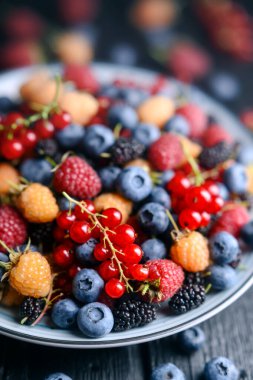 Bir tabakta karışık böğürtlen: yabanmersini, ahududu, kırmızı frenk üzümü, kuşüzümü ve dut. Yemek fotoğrafçılığı