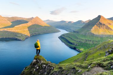 Yalnız turist, muhteşem fiyort Funningur 'a karşı bir uçurumun kenarında duruyor. Eysturoy Adası, Faroe Adaları. Peyzaj fotoğrafçılığı