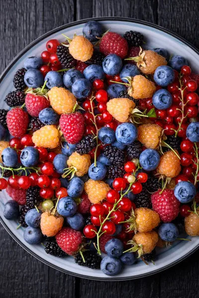 Çeşit çeşit böğürtlen: yaban mersini, ahududu, kırmızı frenk üzümü, kuşüzümü ve bir tabakta dut. Üst manzara, düz yatak, yakın çekim.