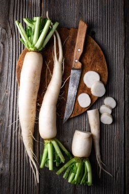 Beyaz daikon turp kökleri, bıçak ve yuvarlak tahta tahtayla yakın plan. Yemek fotoğrafçılığı