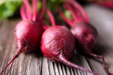 Tahta bir masanın üzerinde yaprakları olan üç taze taze pancar. Yemek fotoğrafçılığı