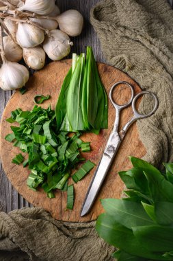Tahta kesme tahtasının üzerinde makasla kesilmiş taze sarımsak yaprakları. Yemek fotoğrafçılığı. Üst görünüm