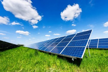 Güneşli bir günde yeşil çayır üzerindeki güneş panelleri. Arka planda bulutlar olan mavi gökyüzü. Alternatif enerji kavramı