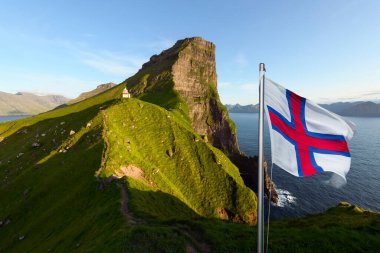 National Faroese flag waving against a background of Kallur lighthouse on green hills of Kalsoy island, Faroe Islands, Denmark. Landscape photography clipart