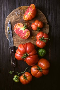 Yuvarlak kesim tahtasıyla olgun kırmızı domatesler, eski bıçak ve kırsal ahşap masa. Yemek fotoğrafçılığı