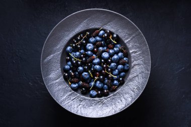 Taze yaban mersinleri, kuşüzümü ve siyah arka planda siyah bir tabakta dut. Yemek fotoğrafçılığı