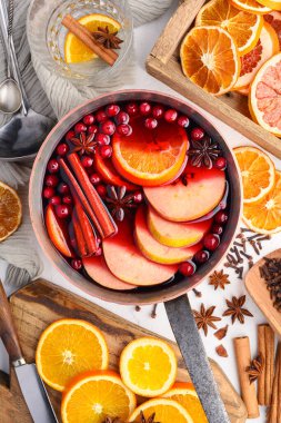 Kırmızı şarapla dolu bakır kap portakal, elma, tarçın, yıldız anason, biberiye ve kızılcık dilimleri ahşap masada. Yemek fotoğrafçılığı