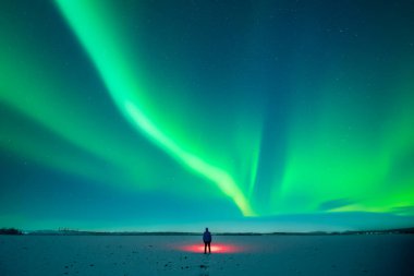 Kırmızı fenerli turist, Aurora Borealis ile yıldızlı gökyüzünün arka planında karlı alanda duruyor. Kutup ışıklarıyla muhteşem bir gece manzarası. Kuzey ışıkları kış tarlasında