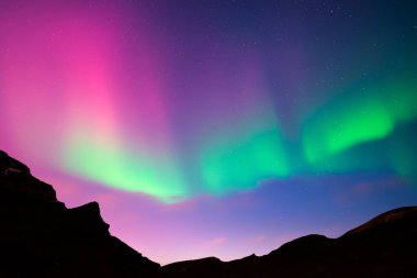 Gece gökyüzü mor Aurora borealis Kuzey ışıkları ile kış dağlarında. Kutup ışıklarıyla gökyüzü ve karanlık tepeli yıldızlar. Peyzaj fotoğrafçılığı