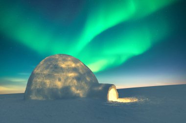 Karlı igloo, Aurora Borealis 'in yeşil dalgalarıyla inanılmaz yıldızlı gökyüzünün arka planına karşı içeriden aydınlandı. Kutup ışıkları. Kuzey ışıkları kış tarlasında.
