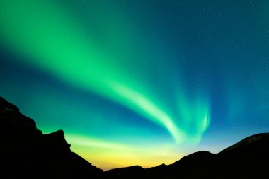 Aurora borealis kış dağlarında kuzey ışıkları. Kutup ışıklarıyla gece gökyüzü ve karanlık tepeli yıldızlar. Peyzaj fotoğrafçılığı