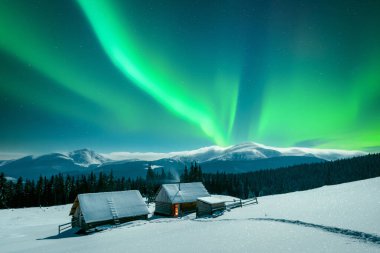 Kuzey ışıkları ve inanılmaz gece gökyüzünün altında, karlı dağlarda yapayalnız ahşap kulübeler olan bir kış sahnesi. Aurora borealis. Noel tatili ve kış tatili konsepti