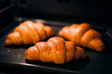 Ev fırınında üç tane kruvasan pişiyor. Yakın çekim. Yemek fotoğrafçılığı