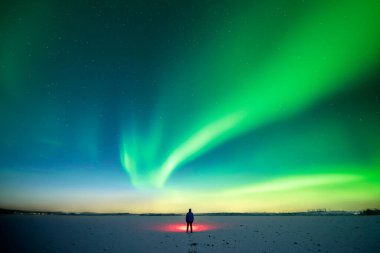 Kırmızı fenerli bir adam, Aurora Borealis ile yıldızlı gökyüzünün arka planında karlı alanda duruyor. Kutup ışıklarıyla muhteşem bir gece manzarası. Kuzey ışıkları kış tarlasında