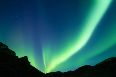 Gece gökyüzü yeşil Aurora borealis kuzey ışıkları kış dağlarında. Kutup ışıklarıyla gökyüzü ve karanlık tepeli yıldızlar. Peyzaj fotoğrafçılığı