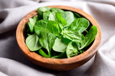 Bir yığın ıspanak yaprağı ve keten masa örtüsünün üzerindeki ahşap kasede su damlaları. Çiğ organik ıspanak yeşillikleri kapanıyor.