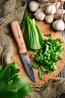 Tahta kesme tahtasındaki yabani sarımsak yapraklarını yakın çekimde bıçakla taze organik ayılar kesiyor. Yemek fotoğrafçılığı