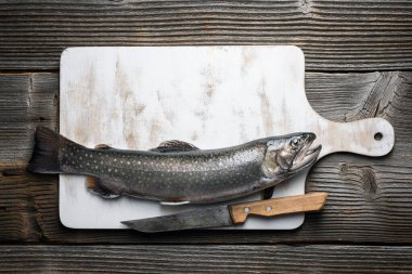 Beyaz ahşap tahta üzerinde kutup balığı, kırsal masada bıçakla doğranmış. Tatlı su nehri alabalığı yaklaşıyor. Yemek fotoğrafçılığı