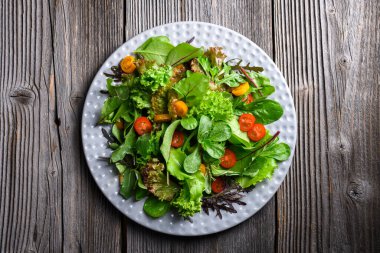 Kırsal ahşap bir yüzeyde organik yeşillikler ve canlı vişneli domateslerle dolu gri bir tabak. Sağlıklı yemek fotoğrafçılığı