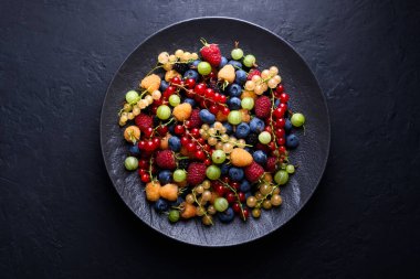Siyah arka planda çok renkli karışık böğürtlenli siyah tabak. Yabanmersini, ahududu, kuşüzümü, kuşüzümü ve dut. Üst manzara, düz uzanma