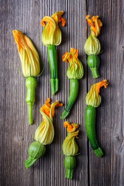 Kırsal ahşap masada çiçekli taze kabak. Taze kabak çiçekleri üstten görünür. Estetik gıda fotoğrafçılığı