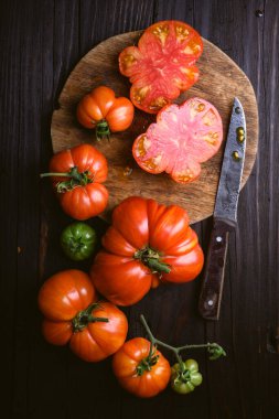 Olgun domatesli kırsal besin bileşimi, yuvarlak ahşap kesme tahtası ve eski model bir bıçak. Yukarıdan aşağıya fotoğrafçılık biçimi