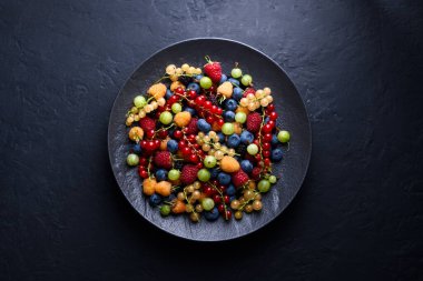 Siyah tabakta çeşitli meyveler. Böğürtlen, ahududu, frenk üzümü, kuşüzümü ve dut. Üst manzara, düz uzanma