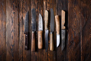 Eski ahşap bir masanın üzerinde duran farklı eski bıçaklar.