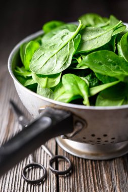 Taze yıkanmış yeşil ıspanak yapraklarını kırsal ahşap masadaki makasla metal kevgire yakın tut. Çiğ organik bebek ıspanağı yığını.