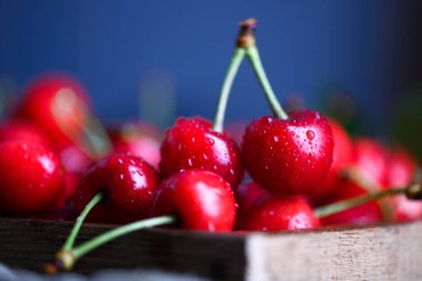 Olgun sulu kırmızı kirazlarla dolu ahşap kutu su damlacıklarıyla kaplanmış. Yemek fotoğrafçılığı