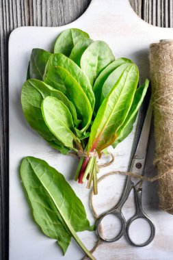 Beyaz ahşap kesme tahtasındaki taze kuş yapraklarının üst görüntüsü. Yemek fotoğrafçılığı