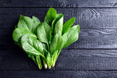 Siyah ahşap masada su damlacıkları olan taze yeşil ıspanak yaprakları. Üst Manzara. Organik ıspanak yeşillikleri. Yemek fotoğrafçılığı