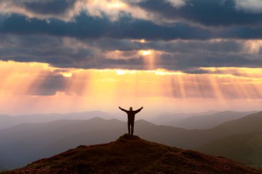 Bir gezgin, rododendron kaplı bir dağın zirvesinde, canlı mor bir gökyüzü, ışınlar ve uzak dağ sıraları ile nefes kesici bir günbatımını hayranlıkla seyrediyor.