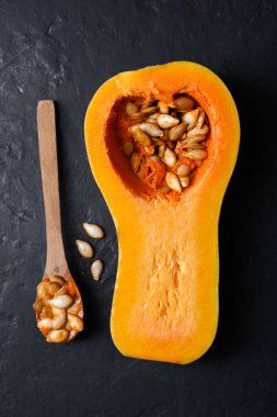 Ahşap kaşık ve siyah masanın üzerinde tohumlar olan çiğ tereyağlı kabak manzarası. Balkabağının yarısı yakın plan. Yemek fotoğrafçılığı