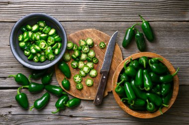 Dilimlenmiş yeşil jalapeno 'nun üst görüntüsü ve yakın çekimde bıçakla ahşap masada. Acı Meksika biberi hazırlıkları. Yemek fotoğrafçılığı