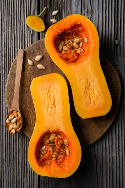 Tahta kesme tahtasının üzerinde tahtadan kaşık ve çekirdekli çiğ tereyağlı kabak manzarası. Balkabağı yarımları yaklaşıyor. Yemek fotoğrafçılığı