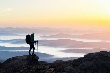 Güneş doğarken sisli dağların arka planında bir sırt çantasının silüetiyle inanılmaz bir manzara. Seyahat ve macera konsepti