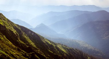 Altın güneş ışınları ve ilkbaharda sisle yıkanmış nefes kesici mavi dağ sıraları. Karpat Dağları. Çarpıcı manzara fotoğrafçılığı.