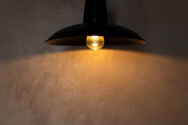 Çatı katı tarzında siyah lambadan gelen sıcak ışıkla beton duvar.