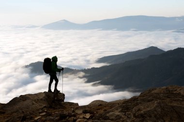 Sisli dağların arkasında sırt çantalı bir yürüyüşçünün silueti. Seyahat ve macera konsepti