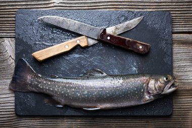 Siyah tahta üzerinde kutup balığı. Kırsal masada iki bıçakla kesme tahtası. Tatlı su nehri alabalığı yaklaşıyor. Yemek fotoğrafçılığı