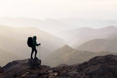 Sırt çantalı bir yürüyüşçünün silueti sisli dağların arka planında. Seyahat ve macera konsepti