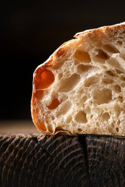 Kırsal ahşap tahtada gözenekli ekmek kırıntıları ve çıtır çıtır deriyle birlikte kırsal ekşi ekmeği bölüm halinde kapatın. Makro ekşi somun dokusu.