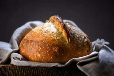 Kırık hamurlu kahverengi ekmek ve ahşap bir masada keten havluya sarılı sert doku. Çiftlik usulü zanaatkar somunu kapat.